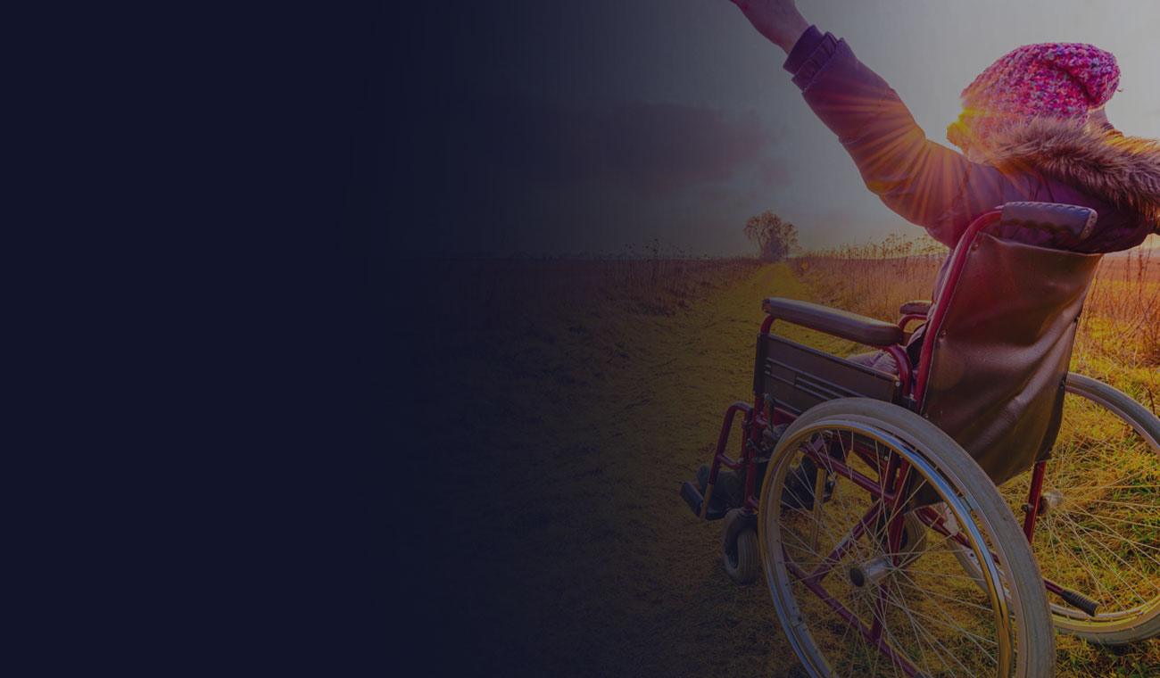 A young woman in a wheelchair is in a field. Her arms are raised  in joy as sunlight falls on her