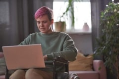 Young disabled woman sitting in wheelchair and typing on laptop computer