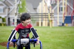 Disabled four year old boy standing in walker near a playground