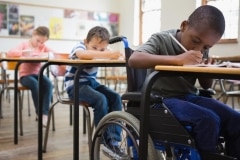 Pupil in wheelchair at writing at desks in classroom