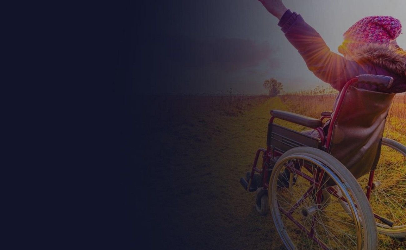 A young woman in a wheelchair is in a field. Her arms are raised  in joy as sunlight falls on her