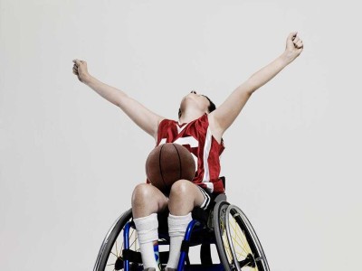 Young lad in wheelchair, a basketball in his lap, hands reaching up in celebration